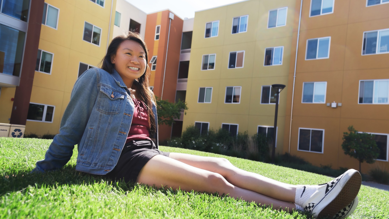 First-generation student, Jenny Hoang, smiling and sitting on Tercero lawn. 