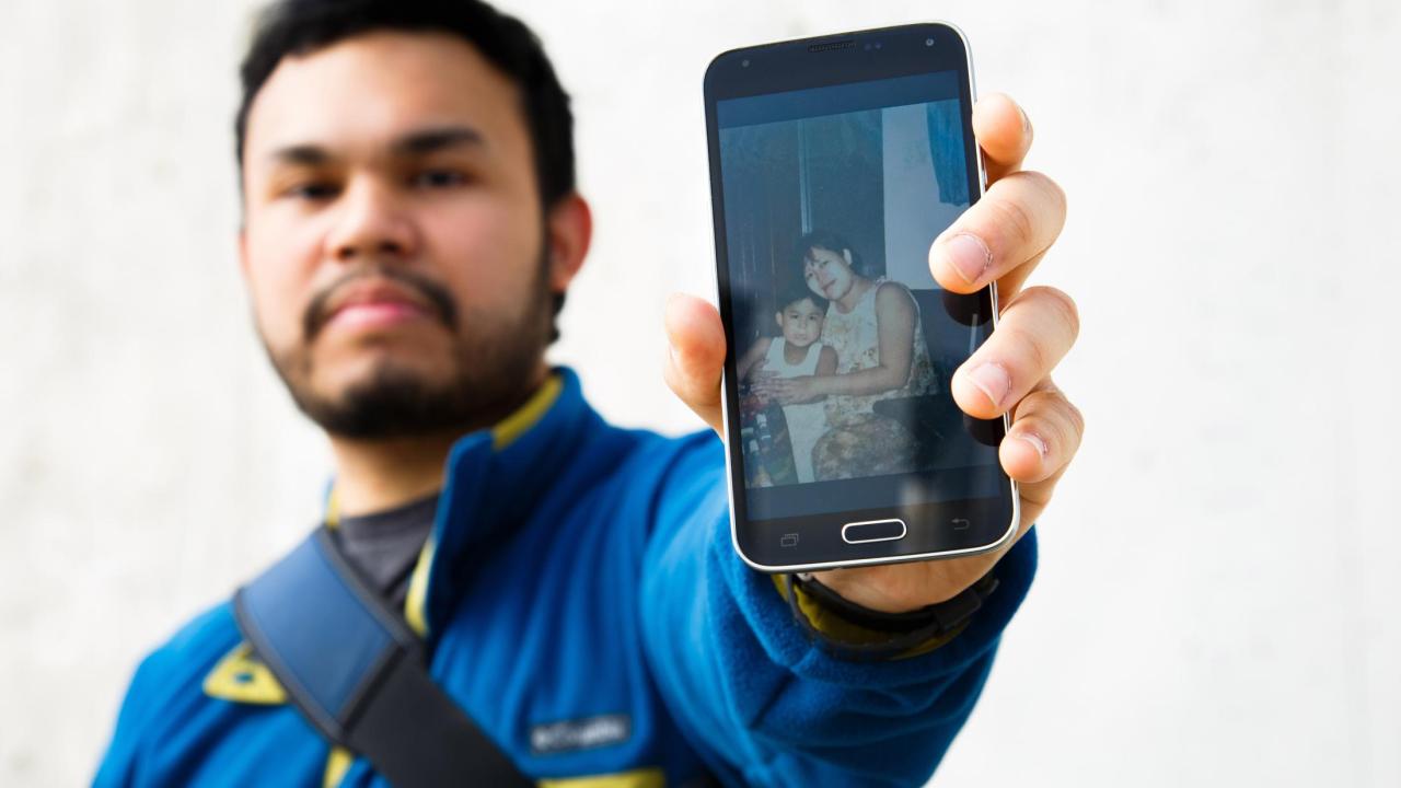 Miguel Flores holding a phone that displays a photo of Miguel with his mom at a younger age