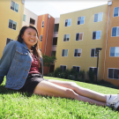 First-generation student, Jenny Hoang, smiling and sitting on Tercero lawn. 